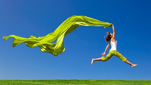 Frau mit grünem Tuch, die über eine Wiese springt