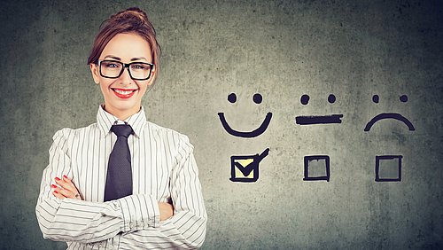 Businessfrau neben drei Emoticons mit freundlichem, mittlerem und unzufriedenem Ausdruck