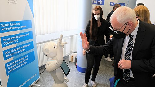 Jürgen Barke, saarländischer Minister für Wirtschaft, Innovation, Digitales und Energie, bei einem High Five mit einem Roboter. Im Hintergrund Nadine Schmidt vom WBV Saarland.