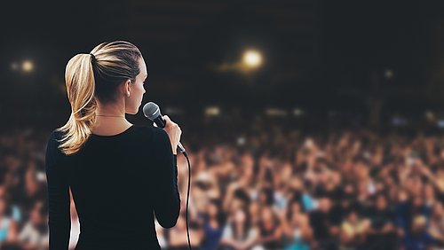 Sprecherin mit Microfon vor einem großen Publikum